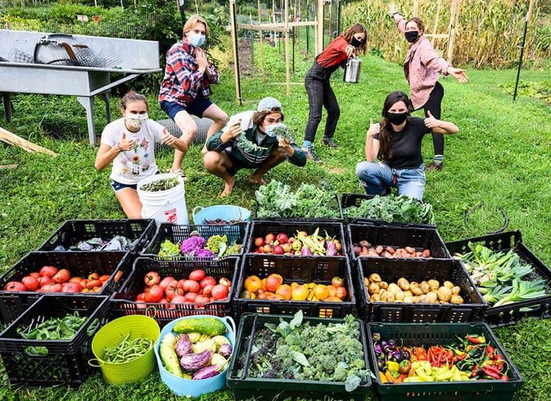 六名学生在鹰高地社区花园收获的数百磅新鲜农产品旁拍照.